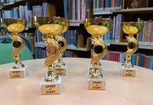 w bibliotece na stole stoją puchary z napisem sport na start